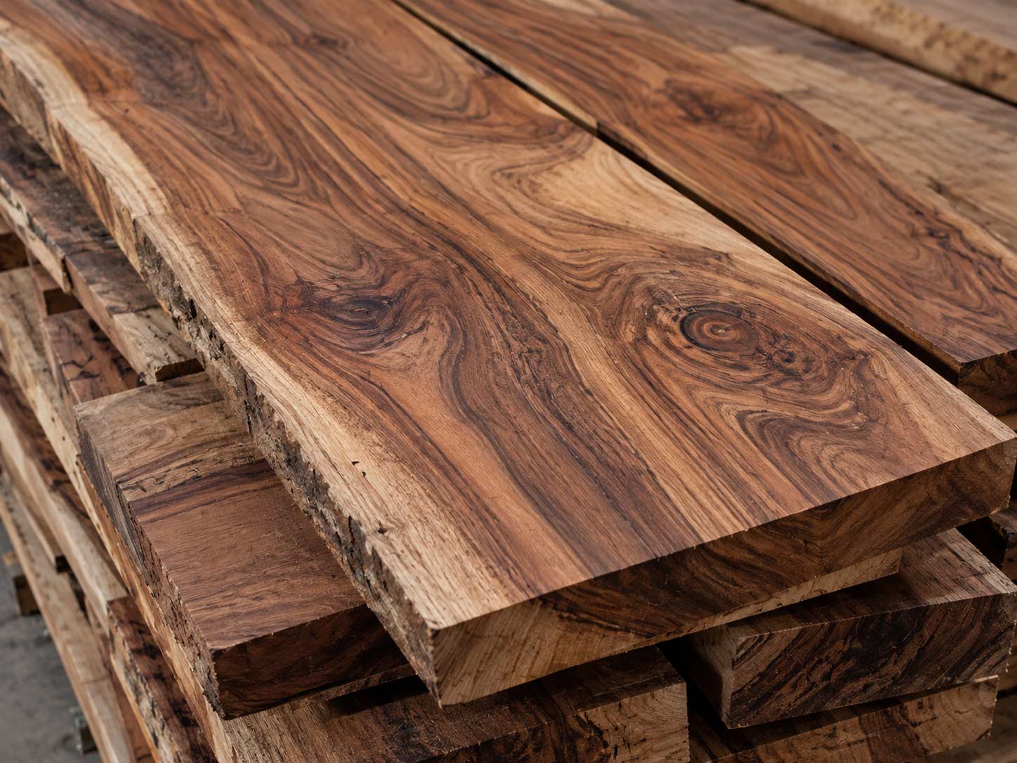 Close-up of raw Sheesham timber boards showing warm brown tones, natural grain variation, knots and unfinished wood texture.